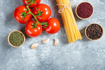 Raw spaghetti, spices and tomatoes on marble background