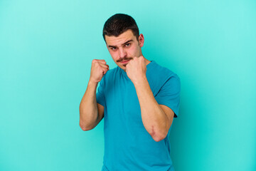 Young caucasian man isolated on blue background showing fist to camera, aggressive facial...