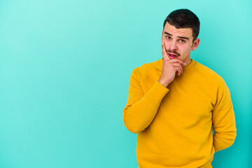 Young caucasian man isolated on blue background looking sideways with doubtful and skeptical expression.