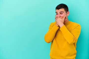 Young caucasian man isolated on blue background thoughtful looking to a copy space covering mouth with hand.