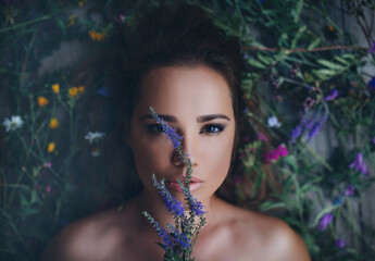Beauty close up portrait of stunning girl lying on wildflowers with flowers around her head. View...