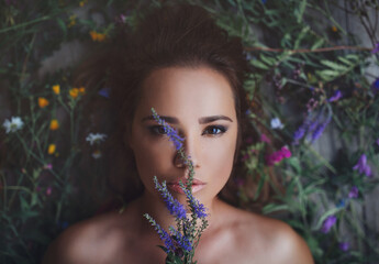 Beauty close up portrait of stunning girl lying on wildflowers with flowers around her head. View from above. Looking  mysteriously. Concept of spring summer youth beauty.  Beautiful face. Romantic - obrazy, fototapety, plakaty