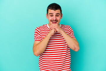 Young caucasian man isolated on blue background keeps hands under chin, is looking happily aside.