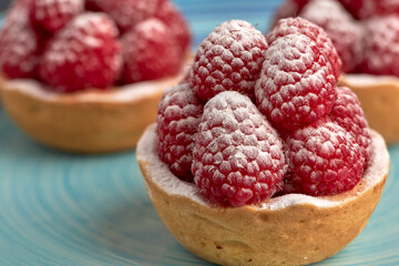 Set of appetizing raspberry tartlets with icing sugar on a spongy sponge base on a wooden table.