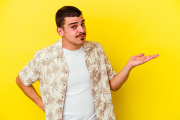 Young caucasian cool man isolated on yellow background doubting and shrugging shoulders in questioning gesture.