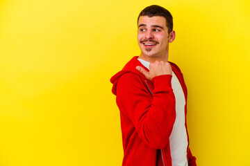 Young caucasian cool man isolated on yellow background points with thumb finger away, laughing and carefree.