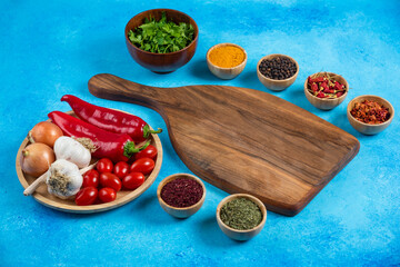 Various spices around wooden board with plate of vegetables