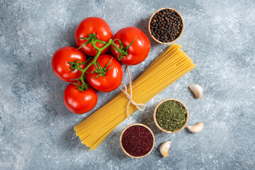 Raw spaghetti, spices and tomatoes on marble background