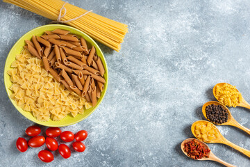 Plate of various pasta, spaghetti and tomatoes on marble background