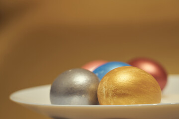 Painted eggs on a white plate with golden background.