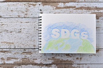 There is a sketch book with "SDGs" written on it. It was an abbreviation for Sustainable Development Goals. It was on top of white damaged wood table.