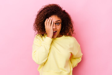 Young african american woman isolated on pink background having fun covering half of face with palm.