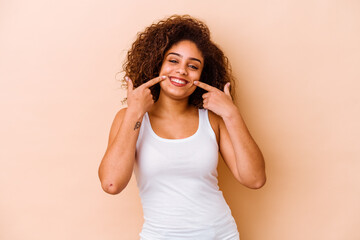 Young african american woman isolated on beige background smiles, pointing fingers at mouth.