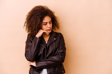 Young african american woman isolated on beige background looking sideways with doubtful and skeptical expression.