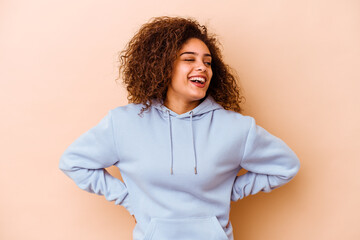 Fototapeta premium Young african american woman isolated on beige background laughs and closes eyes, feels relaxed and happy.