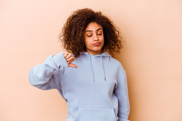 Young african american woman isolated on beige background showing a dislike gesture, thumbs down....