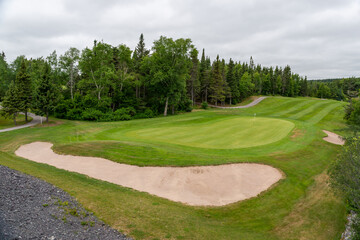 A hole on a golf course with green grass, a sand trap in the shape of a kidney, and lush green...