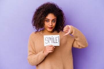 Young African American woman holding a Smile placard isolated on purple background showing a...