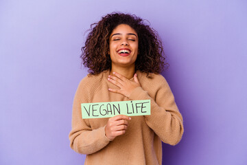 Young African American woman holding a Vegan life placard isolated laughs out loudly keeping hand on chest.