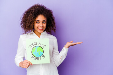 Young African American woman holding a There is no planet B placard isolated showing a copy space on a palm and holding another hand on waist.