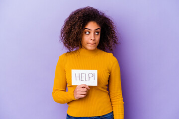 Young African American woman holding a Help placard isolated on purple background confused, feels doubtful and unsure.