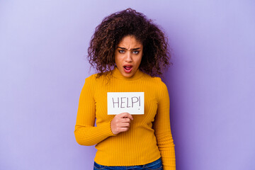 Young African American woman holding a Help placard isolated on purple background screaming very angry and aggressive.