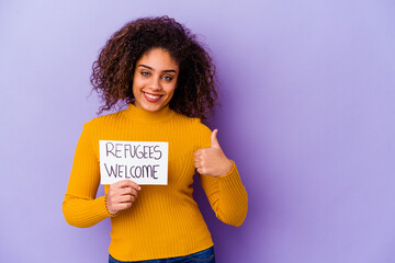 Young African American woman holding a Refugees welcome placard isolated smiling and raising thumb up