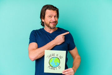 Middle age dutch man holding a there is not planet b placard isolated on blue background smiling and pointing aside, showing something at blank space.