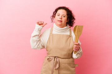 Woman with Down syndrome cooking at home isolated on pink background feels proud and self confident, example to follow.
