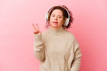 Woman with Down syndrome with headphones isolated on pink background joyful and carefree showing a...