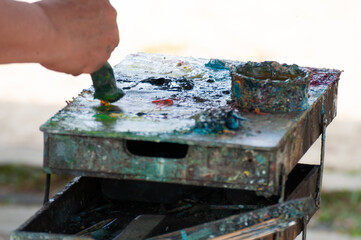 Elderly artist painting on the street. Toning on his palette.