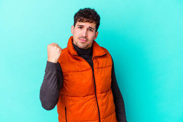 Young caucasian man isolated on blue background showing fist to camera, aggressive facial...