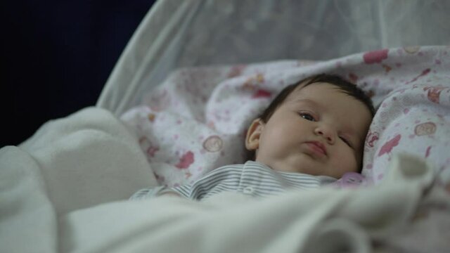 Baby girl rides on a swing at home. Beautiful baby waving pens in a rocking center. 4K slow motion video of home life.