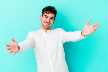 Young caucasian man isolated on blue background feels confident giving a hug to the camera.
