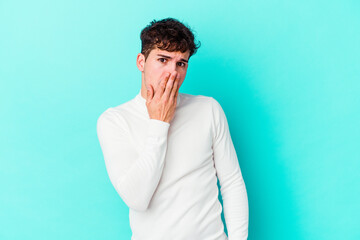 Fototapeta na wymiar Young caucasian man isolated on blue background shocked, covering mouth with hands, anxious to discover something new.