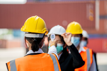 Factory woman worker in a face medical mask and safety dress used measures temperature at worker...