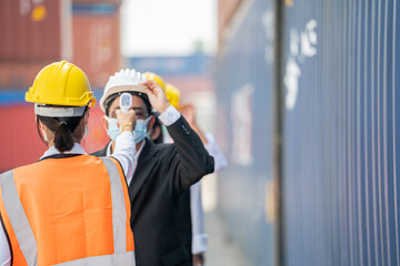 Factory woman worker in a face medical mask and safety dress used measures temperature at worker...
