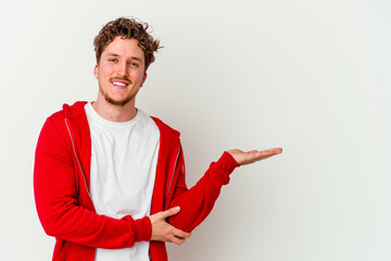 Young caucasian man isolated on white background showing a copy space on a palm and holding another...