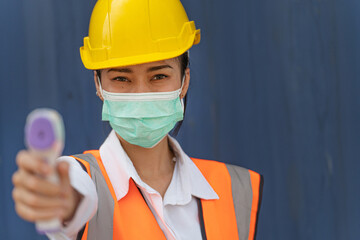 Asian woman worker in mask face and using measures temperature with a non-contact infrared...