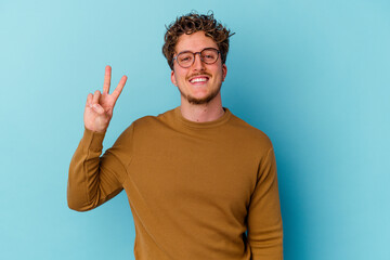 Fototapeta premium Young caucasian man wearing eyeglasses isolated on blue background showing victory sign and smiling broadly.