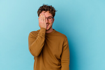 Obraz premium Young caucasian man wearing eyeglasses isolated on blue background having fun covering half of face with palm.