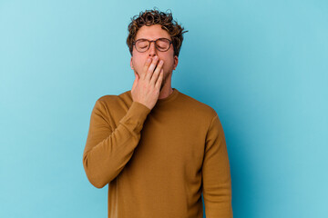 Young caucasian man wearing eyeglasses isolated on blue background yawning showing a tired gesture covering mouth with hand.