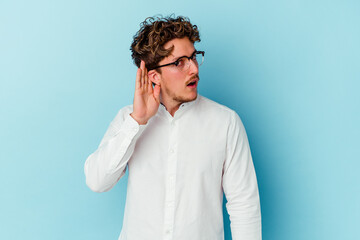 Young caucasian business man isolated on blue background trying to listening a gossip.