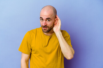 Young caucasian bald man isolated on purple background trying to listening a gossip.