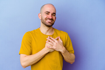 Young caucasian bald man isolated on purple background has friendly expression, pressing palm to chest. Love concept.