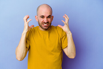 Young caucasian bald man isolated on purple background screaming with rage.