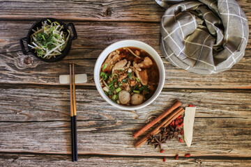 Egg noodle with pork and vegetable in five spices black soup on wooden table top view- Asian food style.