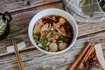 Egg noodle with pork and vegetable in five spices black soup on wooden table top view- Asian food style.