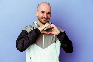 Young caucasian bald man isolated on purple background smiling and showing a heart shape with hands.