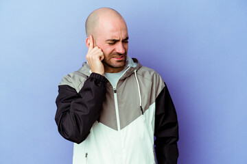 Obraz premium Young caucasian bald man isolated on purple background covering ears with hands.